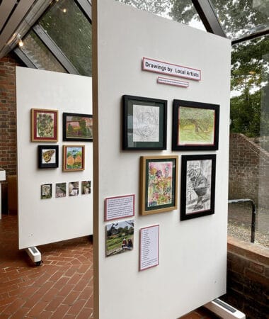 A photograph depicting two boards with the artwork of local artists framed on them at the Harlow museum. The room has large windows which light up the artwork.