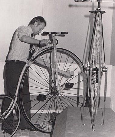 An old photograph of a man handling a penny farthing bicycle