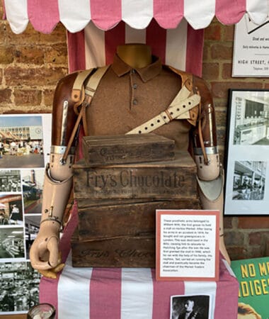 A photograph of a display cabinet with a headless mannequin holding 'Fry's Chocolate' with a description at the Harlow museum.